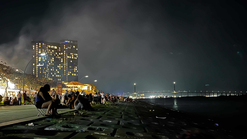 Evening crowd along the seaside boardwalk overlooking city lights at Il Corso
