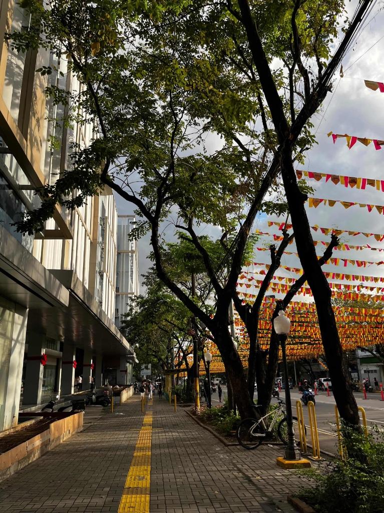 Sunlit street decorated with yellow and red buntings between green trees