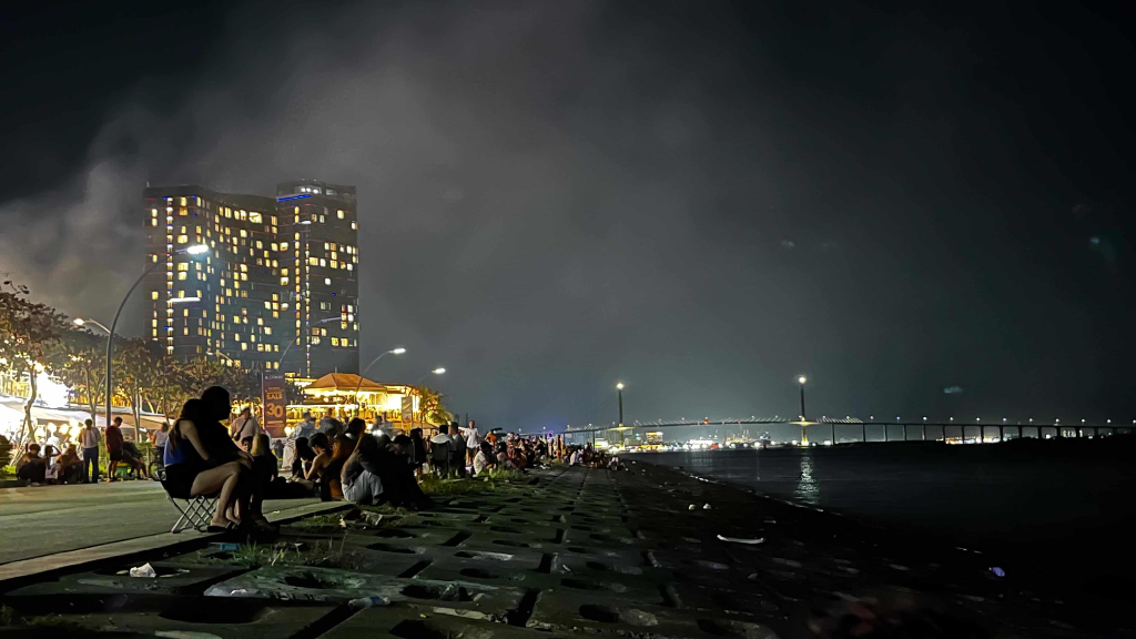 Scenic evening crowd gathering along the seaside boardwalk overlooking the city lights and distant horizon at Il Corso